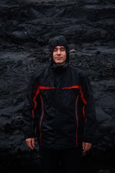 Portrait of a man with eyes closed in a hooded jacket on rugged dark rocks. Travel and exploration theme.