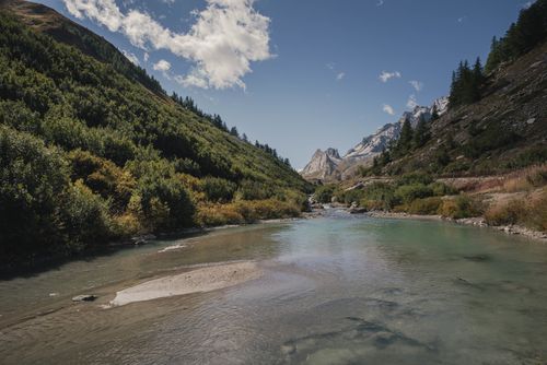 Free A breathtaking view of a serene river flowing through a lush green valley surrounded by majestic mountains under a clear blue sky. Stock Photo