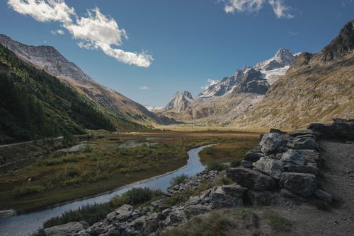 Free Explore the serene beauty of an alpine valley with majestic mountains, clear skies, and a flowing river. Stock Photo