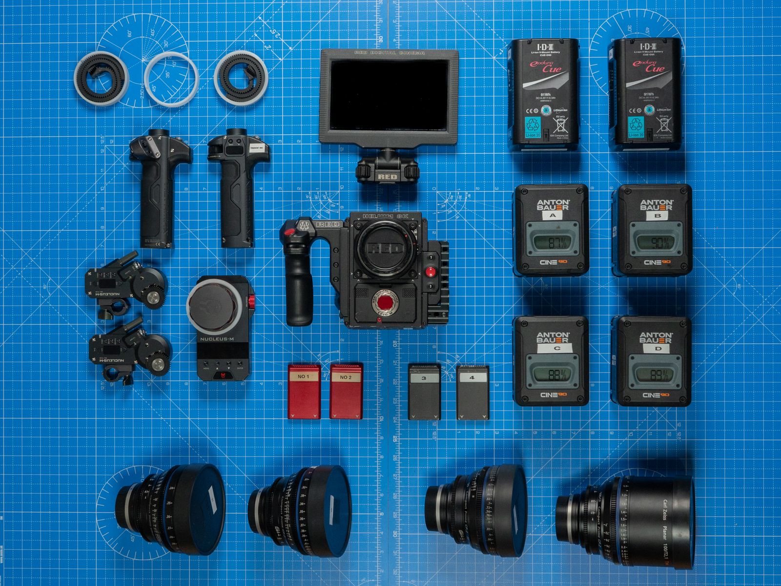 Overhead layout of professional camera gear, lenses, batteries, monitor, and accessories