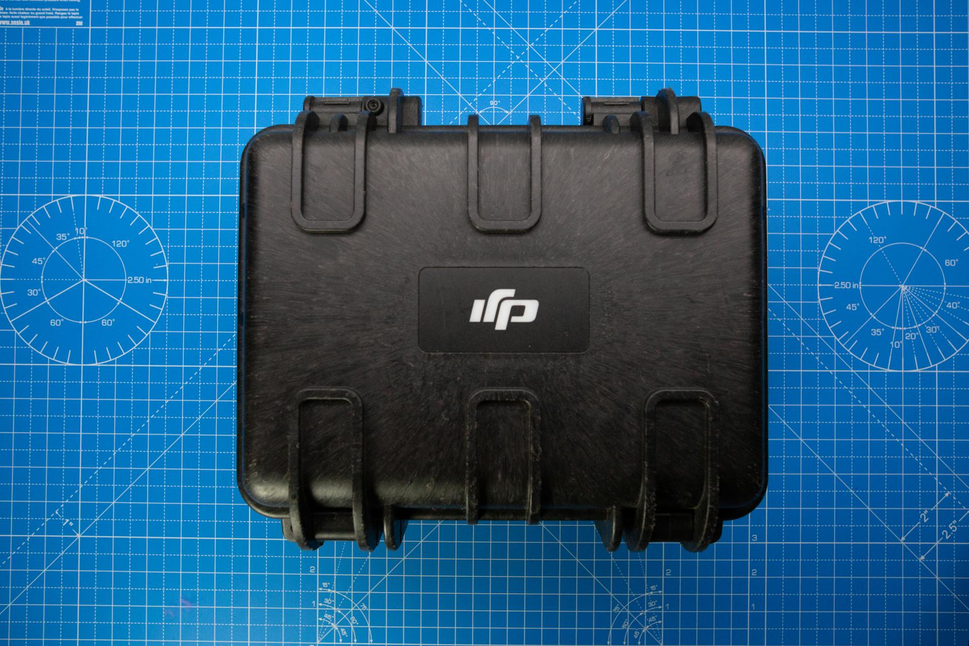 A black protective hard case on a blue grid background, ideal for travel and equipment storage.