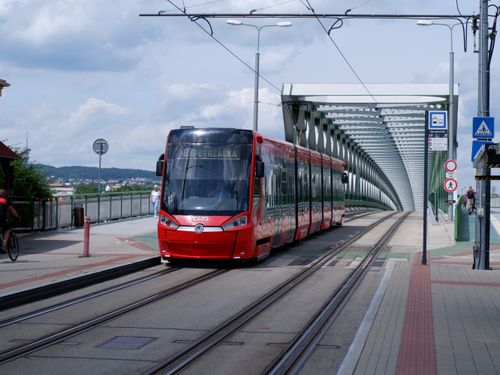 Free A red tram traveling on a modern bridge in a cityscape on a clear day. Stock Photo