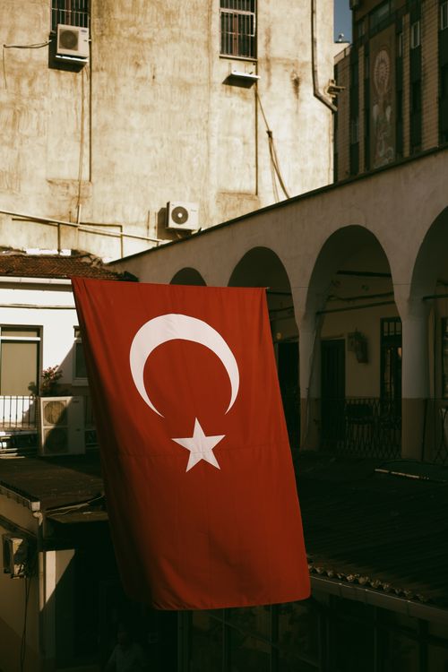 Free Turkish flag waving in front of a historic building in Istanbul, capturing a blend of tradition and urban life. Stock Photo