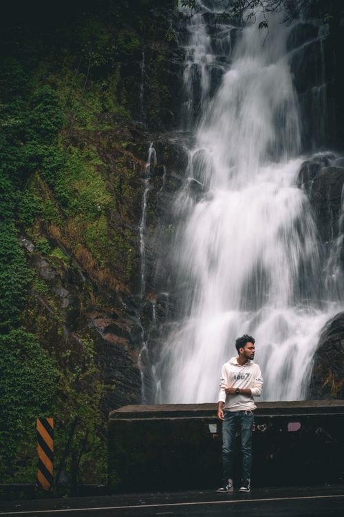 Free A young man stands by a cascading waterfall surrounded by lush greenery in Peruvanthanam, India. Stock Photo