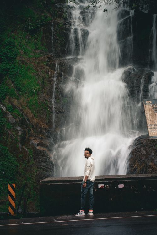 Free Man standing before a cascading waterfall in Peruvanthanam, Kerala, India, embracing nature's beauty. Stock Photo