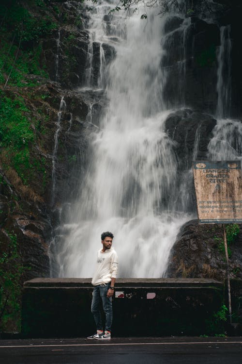 Man in White Hoodie Standing Beside a Waterfalls