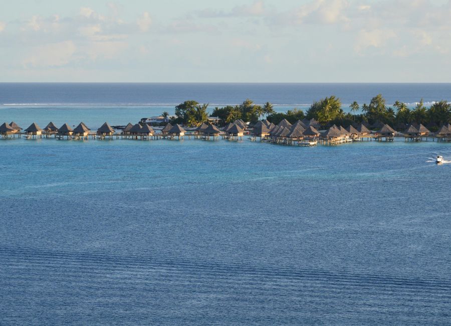 Overwater bungalows on a tropical island with clear blue sea and lush coast.