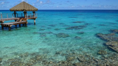 Free A serene view of a wooden hut on a jetty over the clear blue ocean under a bright sky. Stock Photo