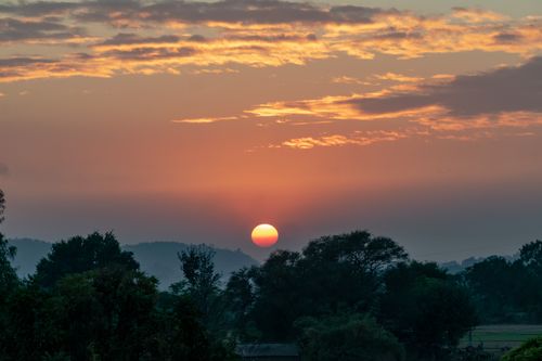 Free A serene view of a sunset with silhouetted trees and vibrant clouds. Stock Photo
