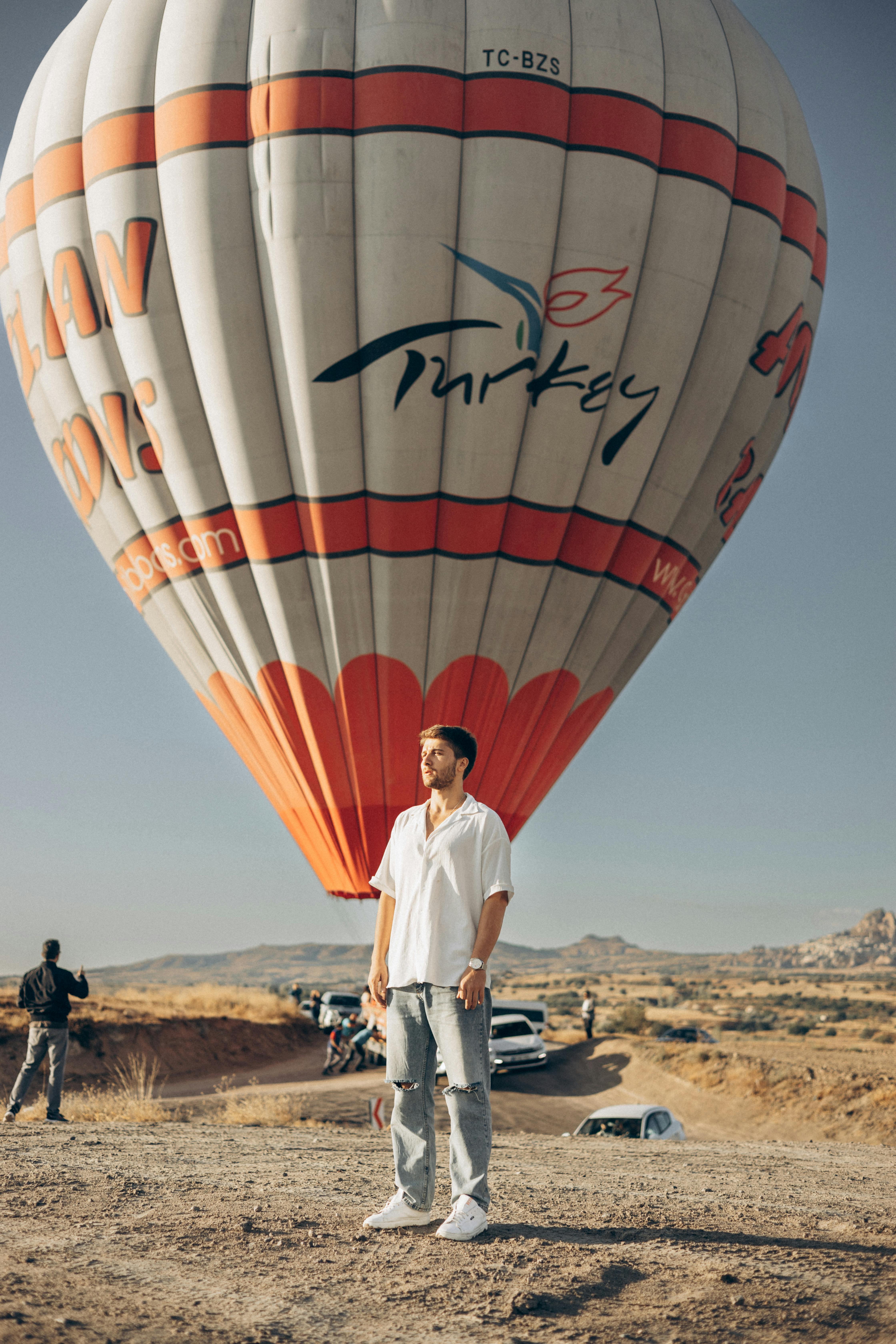 A man stands in front of a hot air balloon on a sunny day in Cappadocia, Turkey.