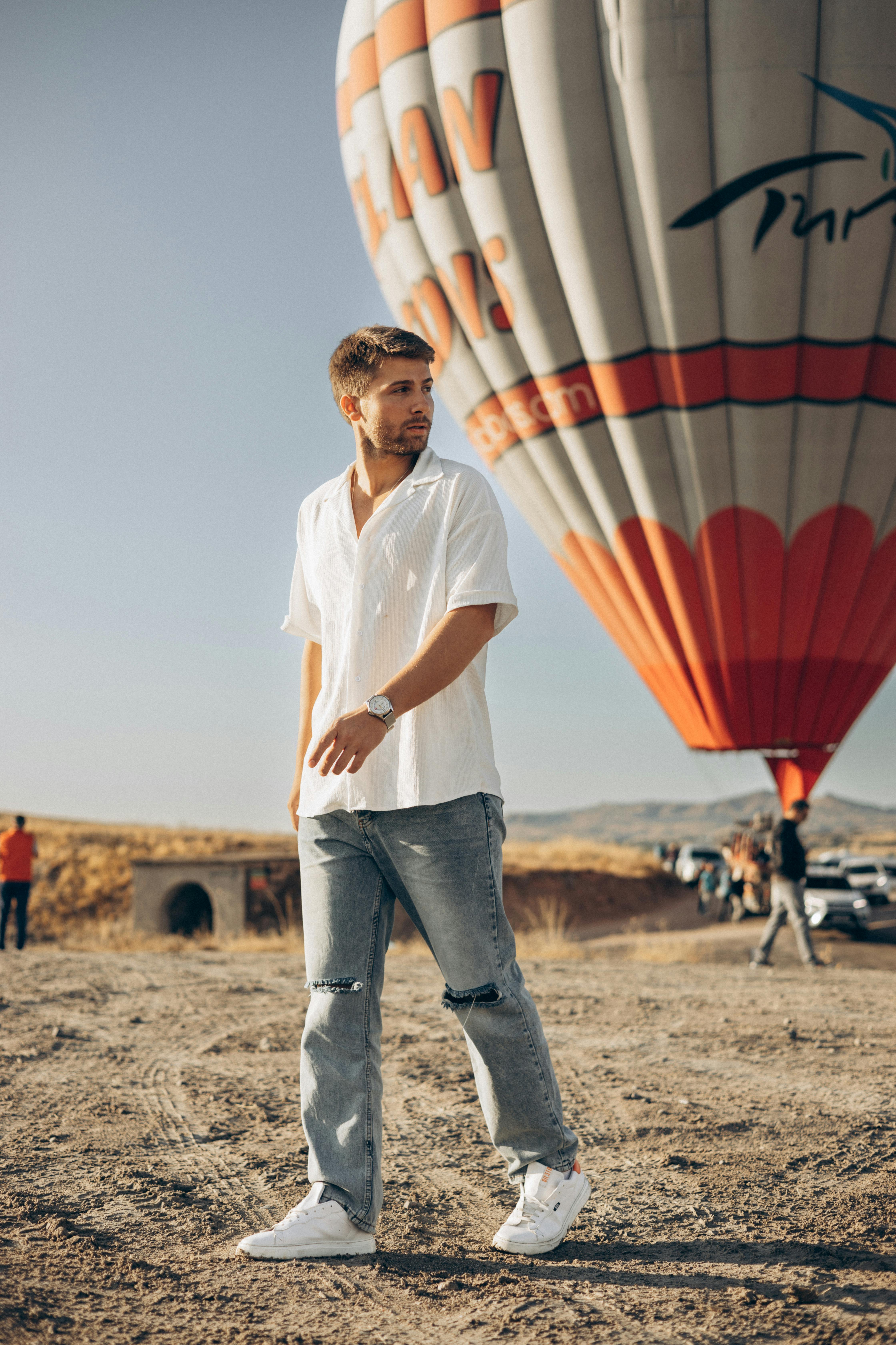 Young man near a hot air balloon in Cappadocia, enjoying a sunny day.