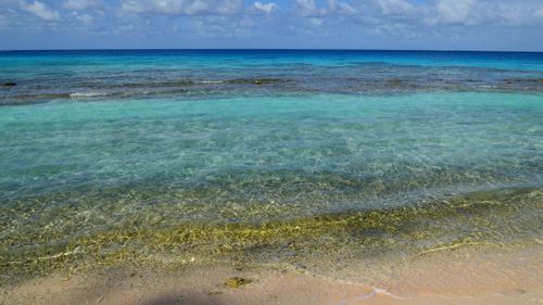 Free Peaceful sandy beach with clear turquoise waters and cloudy skies creating a serene coastal landscape. Stock Photo