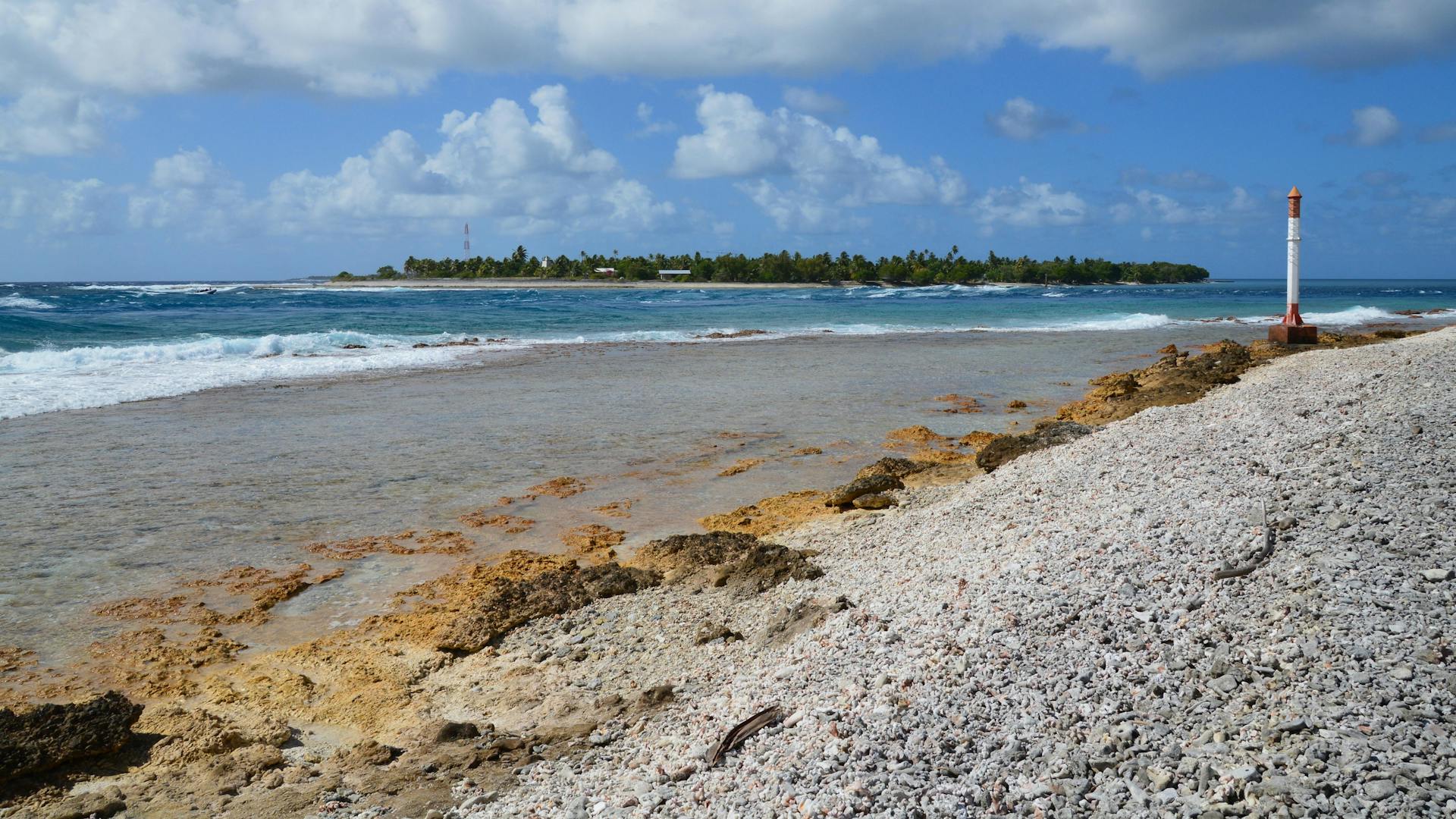Serene beachscape with coral sand and gentle waves under a bright sky, featuring a distant island.