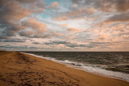 Free Peaceful beach scene at dusk with ocean waves, sandy shore, and cloudy sky. Stock Photo