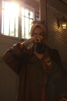 A woman in a hijab photographing indoors with natural light.