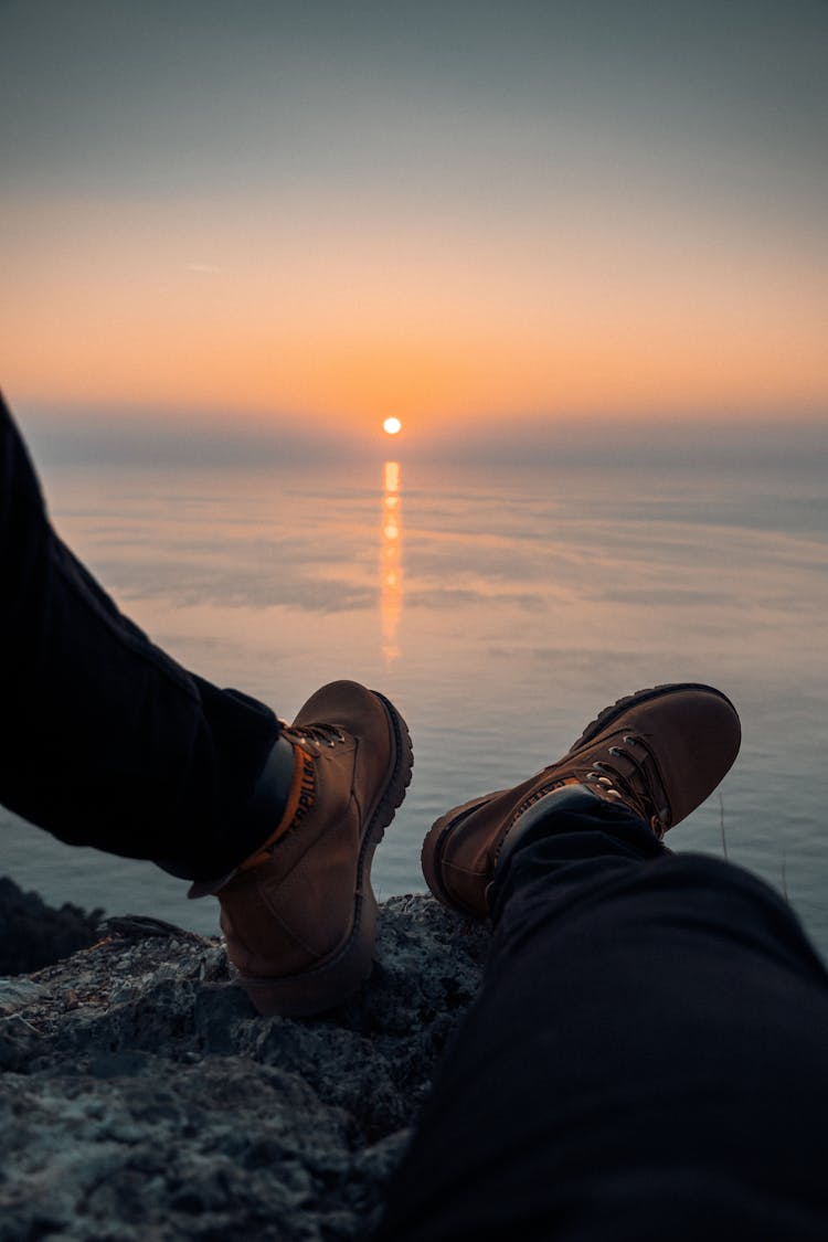 A Person Wearing Brown Leather Shoes Sitting On Rock During Sunset