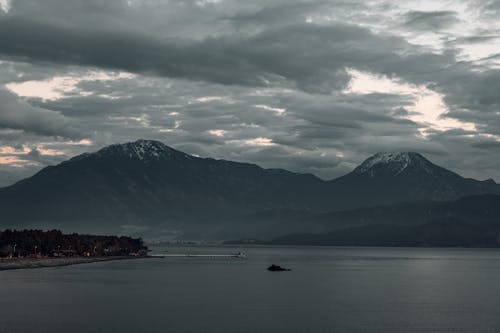 Body of Water Near Mountain Under Cloudy Sky