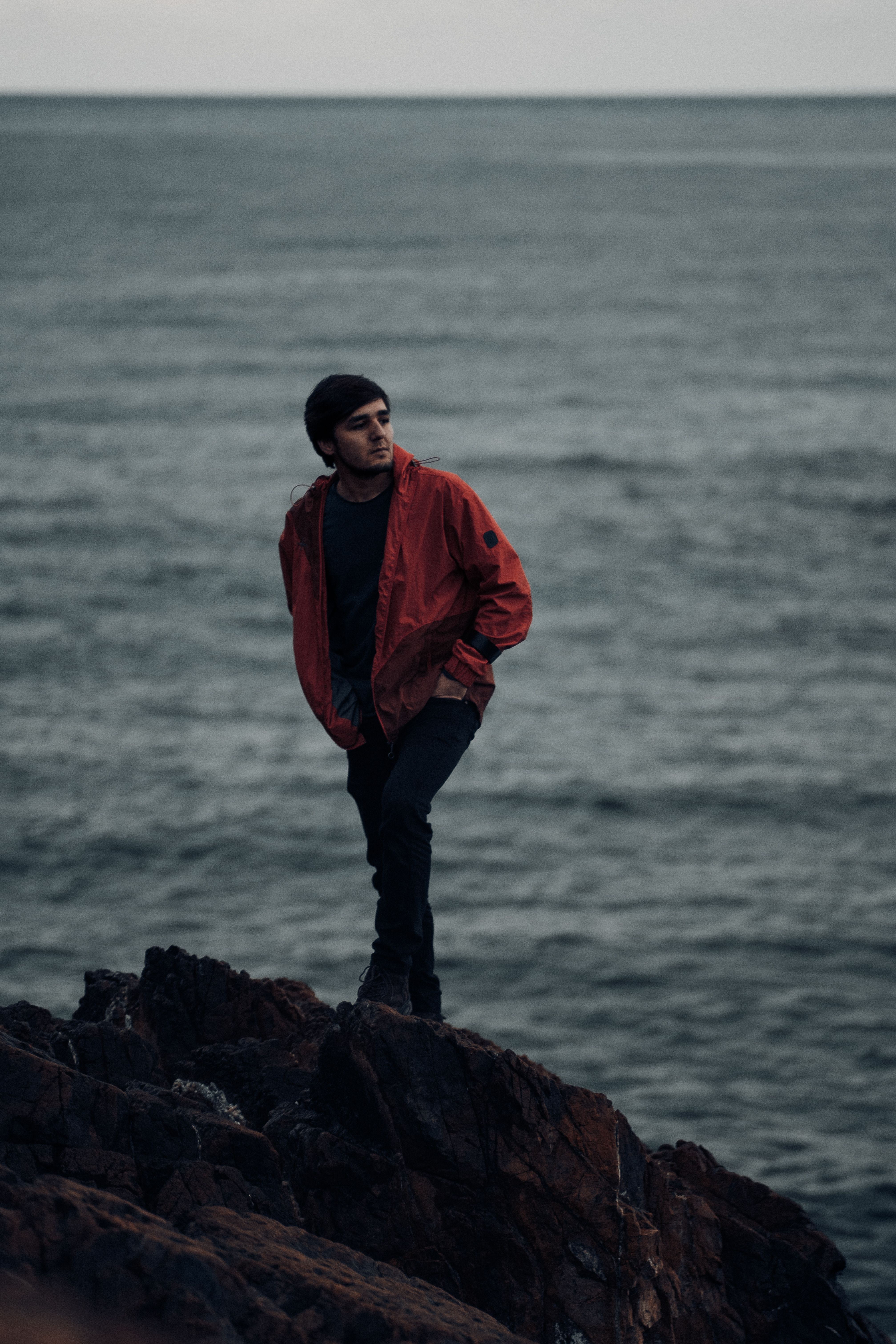 A Man in Orange Jacket Standing on Rock Near Body of Water · Free Stock ...