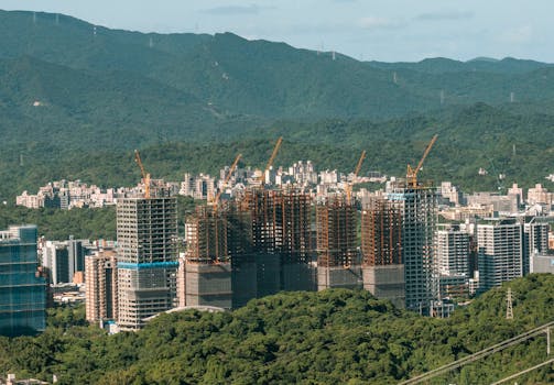 Aerial view of urban construction with cranes set against a mountain backdrop.