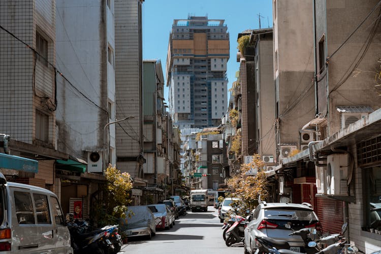 Cars Parked On Side Of The Road In Between High Rise Buildings