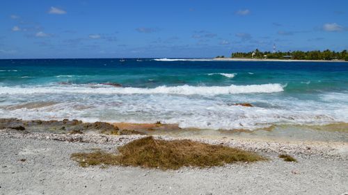 Free Vivid blue waves crash onto the sandy tropical beach under clear skies. Stock Photo