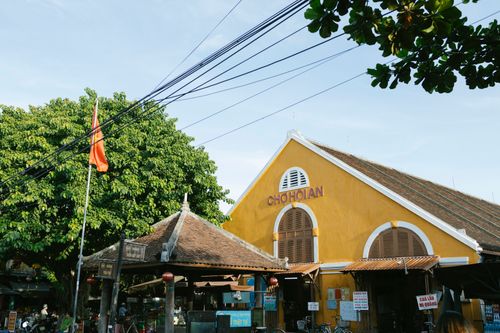 Free A traditional yellow market building in Hoi An, Vietnam, with lush greenery and a Vietnamese flag. Stock Photo