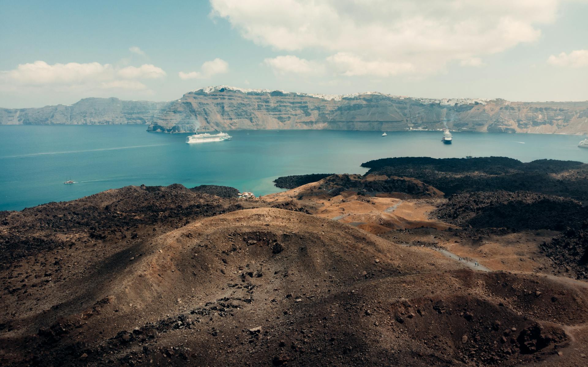 A stunning aerial view of the Santorini caldera with cruise ships and volcanic landscape under a clear sky.