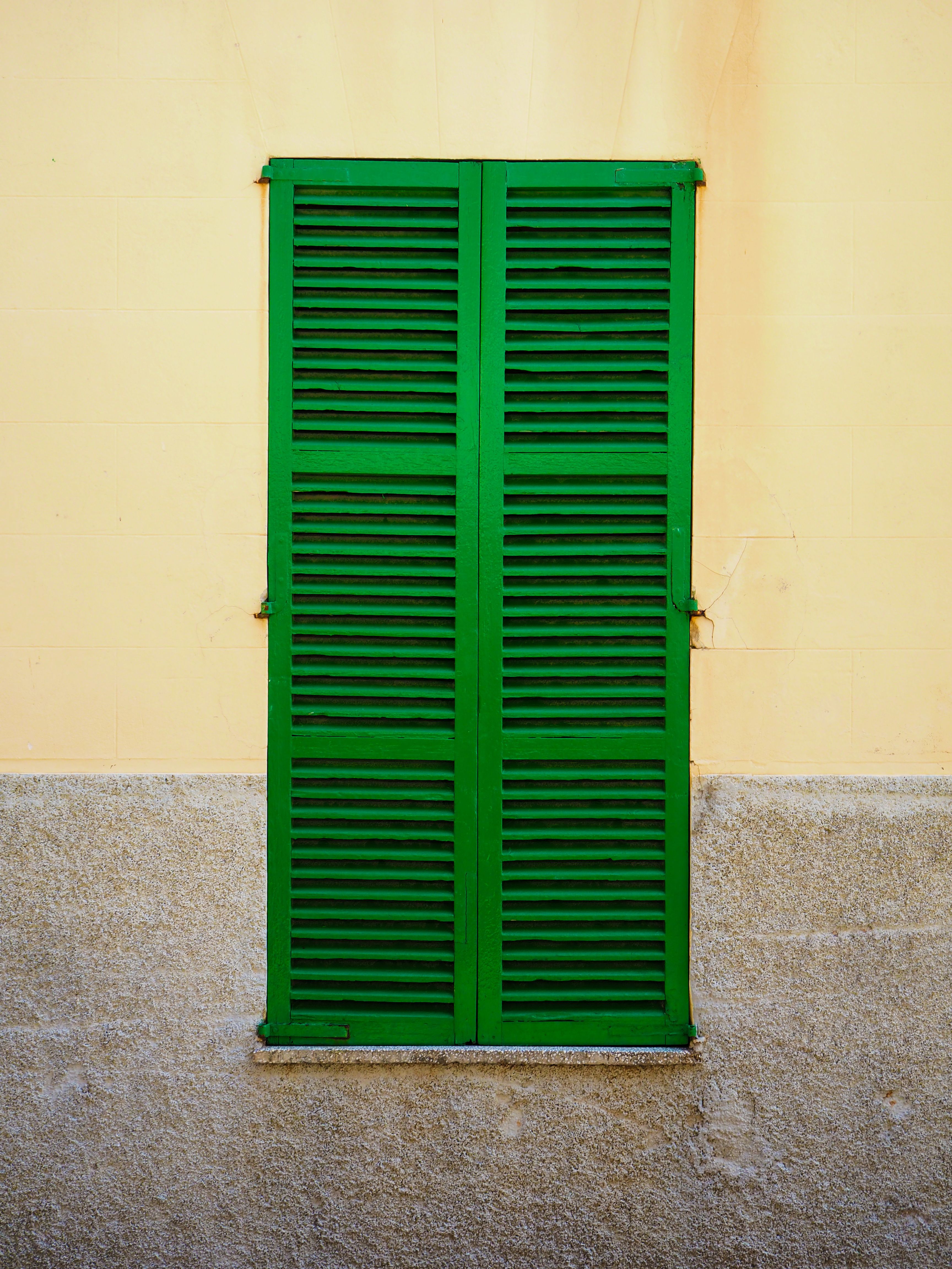 Bright green shutters on a yellow wall captured in Palma de Mallorca, Spain. A striking architectural detail.