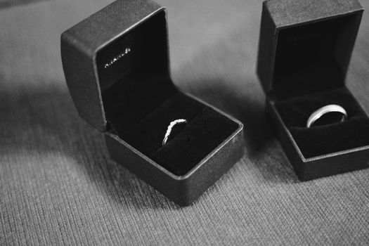 A black-and-white close-up of two wedding rings in elegant open boxes on a textured surface.
