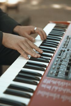 An adult musician's hands playing an electronic keyboard outdoors in natural light.