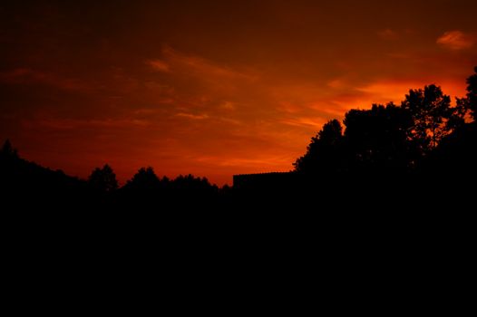 A stunning red sunset sky silhouettes the surrounding trees creating a dramatic scene.