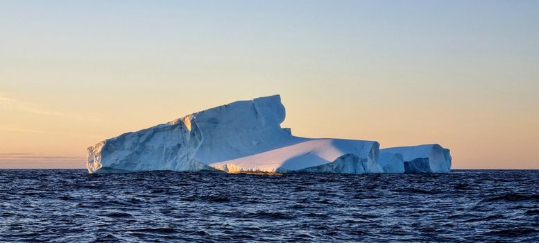 A stunning view of a large iceberg floating in open water during sunset, emphasizing natural beauty.