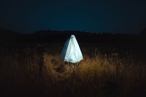 Free Eerie ghost in a white sheet standing alone in a dark field under a night sky. Perfect for Halloween imagery. Stock Photo