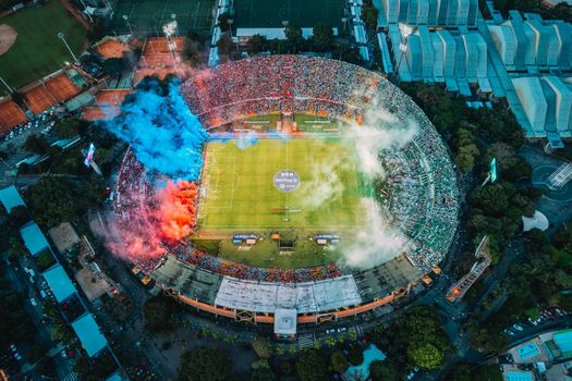Dynamic aerial shot of a packed stadium in Medellín, Colombia with colorful smoke displays.