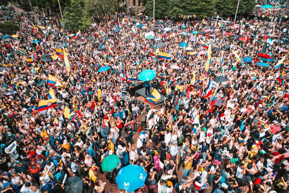 Vista aérea de un colorido desfile en Bogotá, Colombia, con una gran multitud agitando banderas.