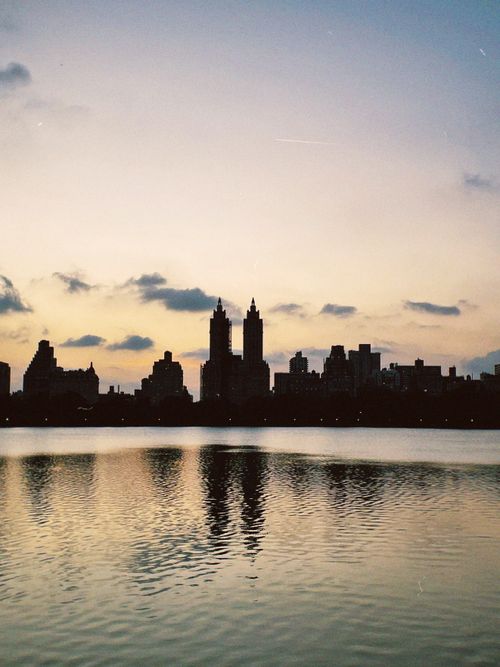 Free Serene view of the NYC skyline silhouette at sunset with golden reflections on the water. Stock Photo