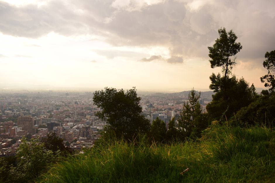 An expansive view of Bogotá cityscape beneath dramatic evening skies, framed by lush green hillsides.