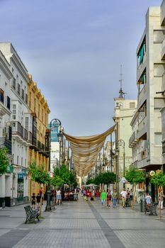 A vibrant day on a pedestrian street in Sanlúcar de Barrameda, showcasing urban architecture and street life.