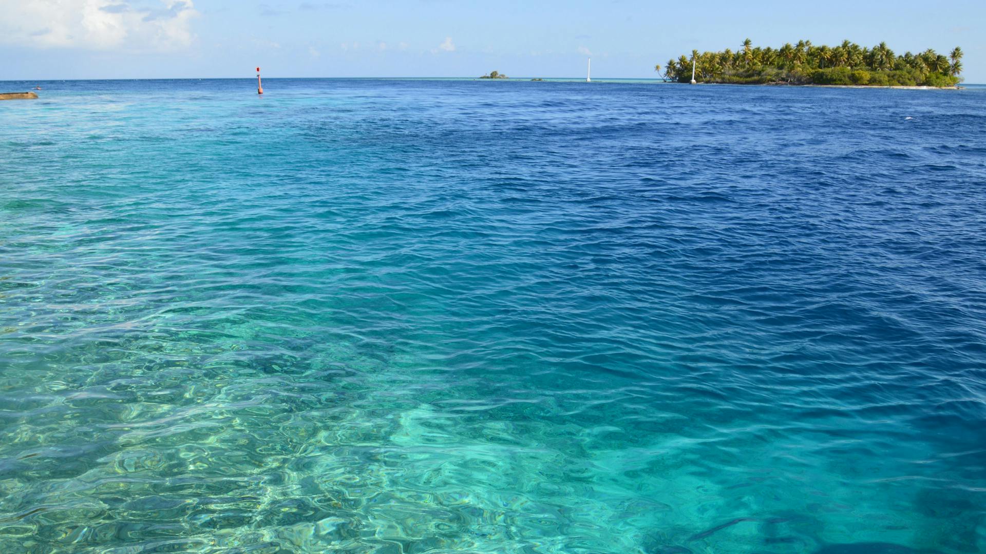 Crystal clear turquoise waters with a distant tropical island under a bright blue sky.