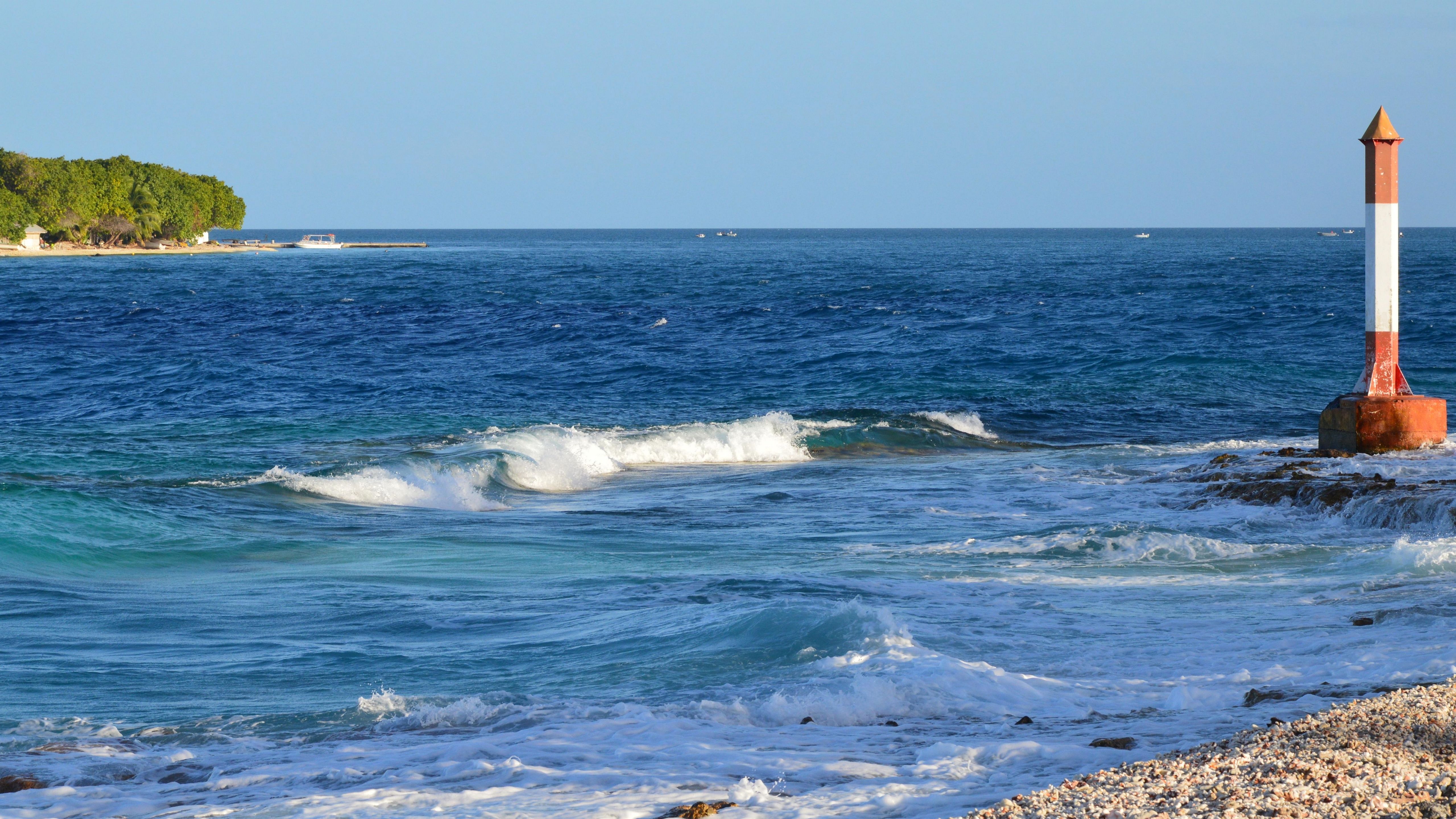 Ocean waves crashing near a coastline under a clear blue sky.