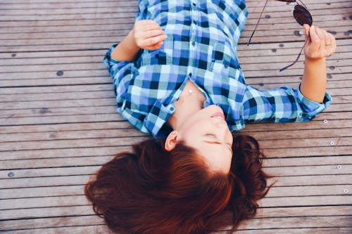 Woman Lying on Wooden Surface Holding Sunglasses