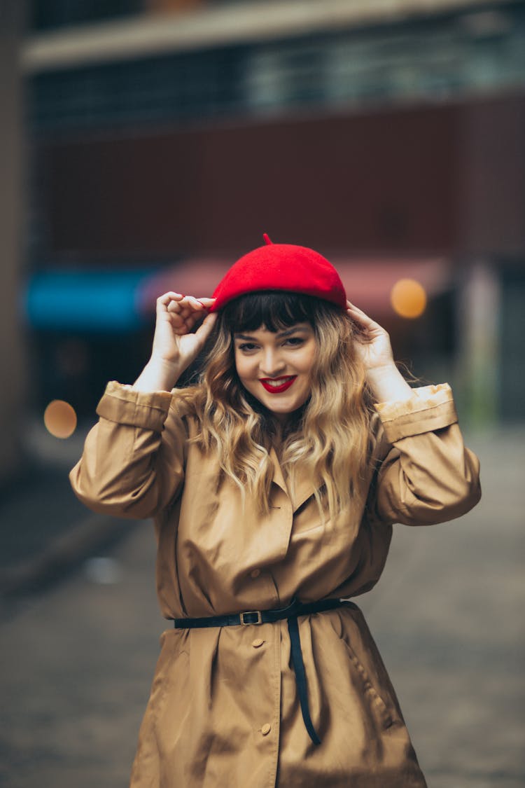 Woman In A Trench Coat Standing And Fixing Her Red Beret 