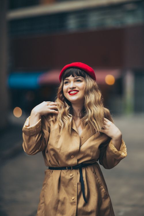 Free Fashion portrait of a woman in a red beret and trench coat, soft urban background. Stock Photo