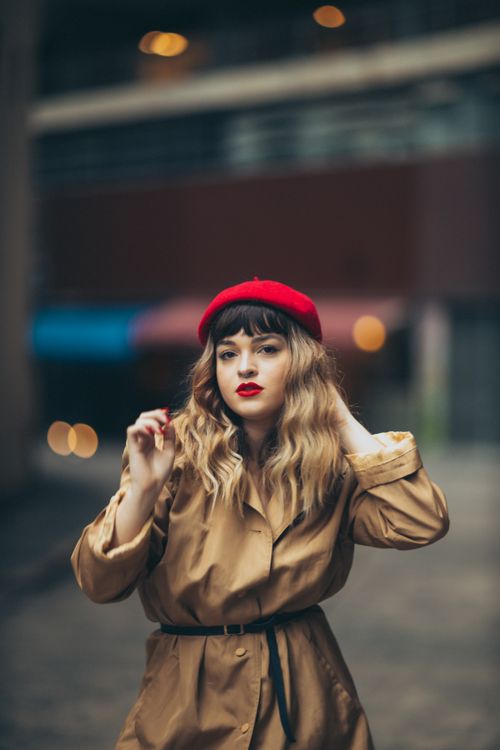 Free Stylish woman in trench coat and red beret fixing hair outdoors, showcasing fashion and elegance. Stock Photo