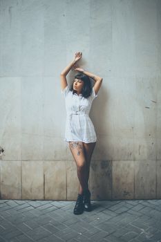 Fashionable woman in white jumpsuit posing with arms raised outdoors.