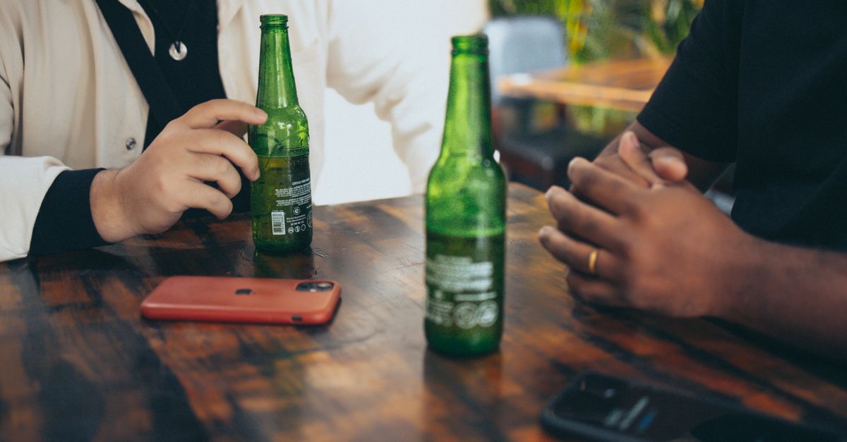 Two individuals having a casual conversation with beer bottles and smartphones on a wooden table.