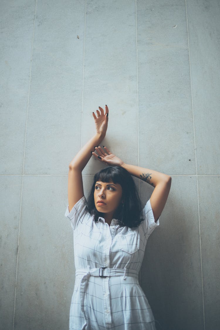 Woman Standing Under Wall With Hands Raised Above Head