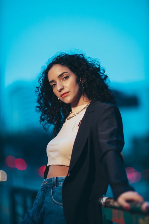 Free Portrait of a stylish woman with curly hair in a city at twilight. Stock Photo