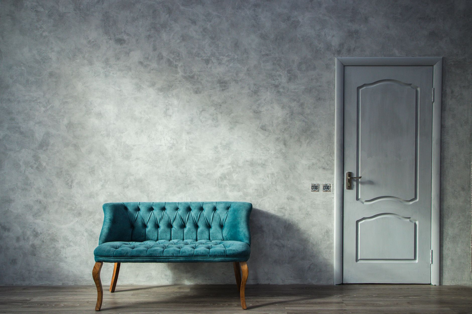 Elegant minimalist interior with a teal sofa and a white door against a grey wall.