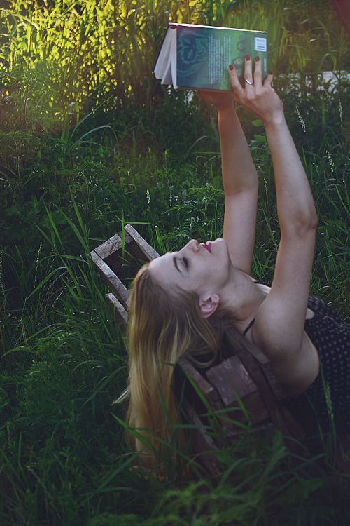 Free Young woman with blonde hair reading a book in a serene outdoor setting. Stock Photo